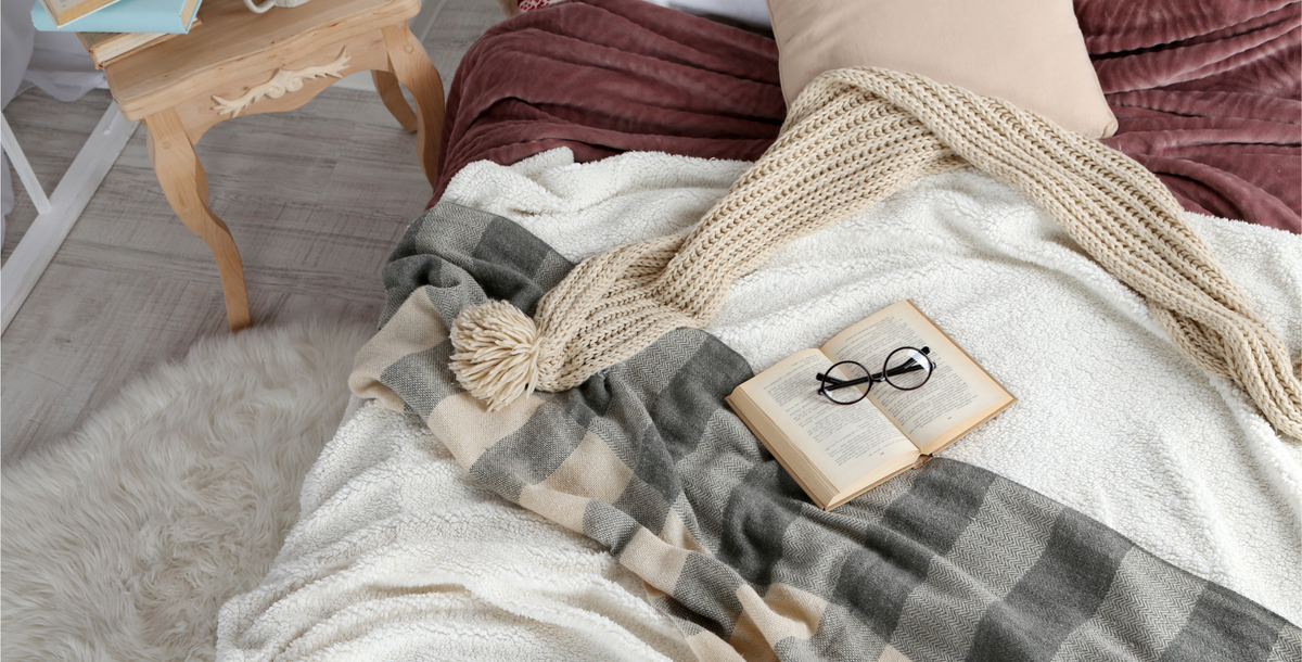 Book with reading glasses laid on an unmade bed